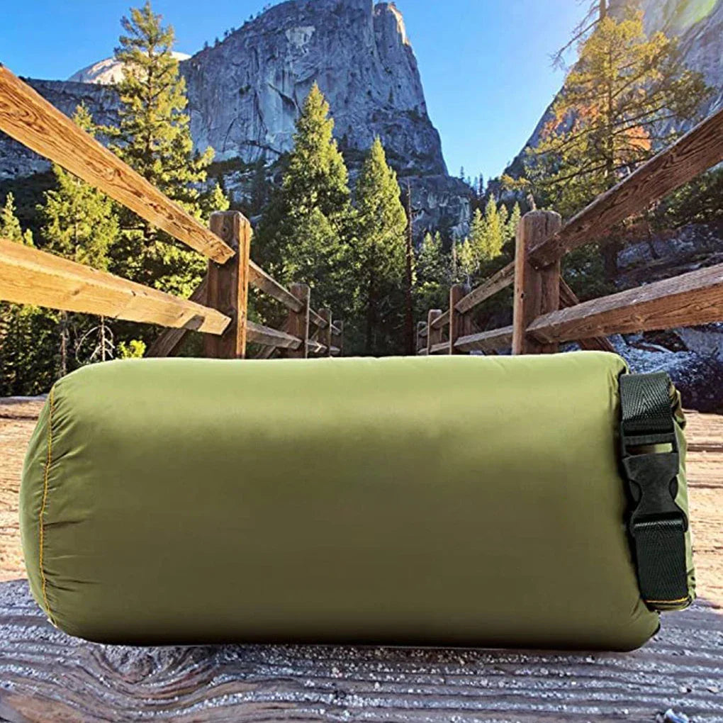 Adventure Cozy Puff Ultralight Blanket rolled into its green compression sack on a wooden surface with mountains in the background