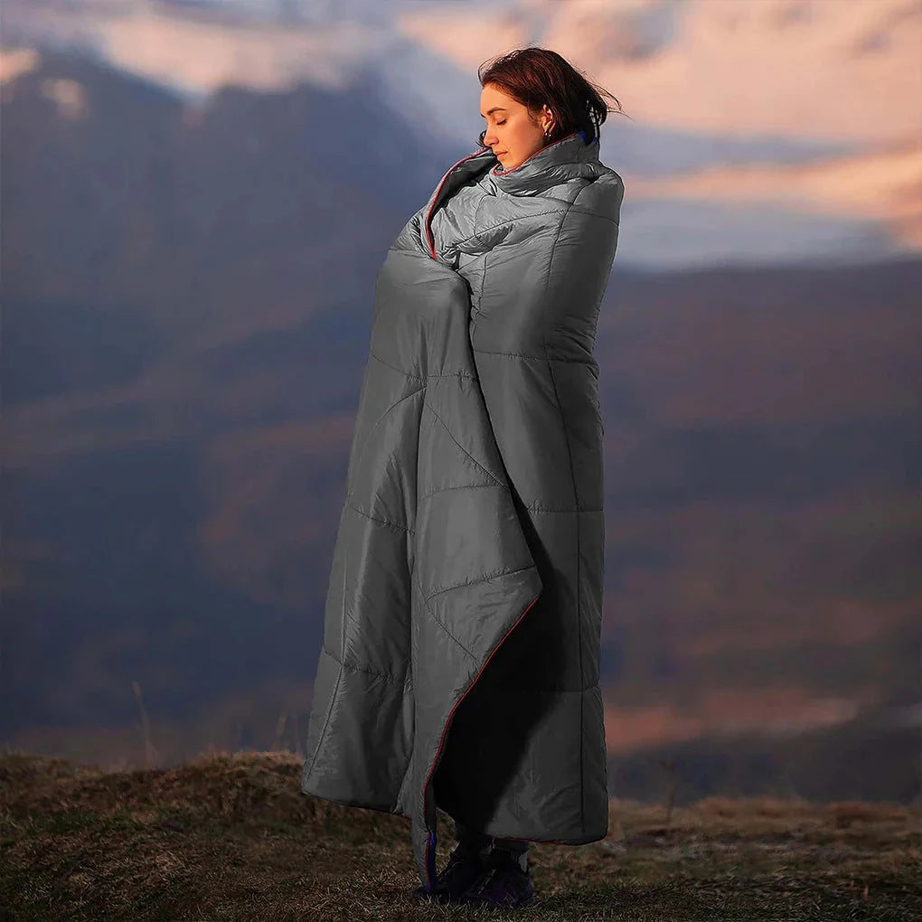 Woman standing outdoors in the mountains wrapped in the Adventure Cozy Puff Ultralight Blanket